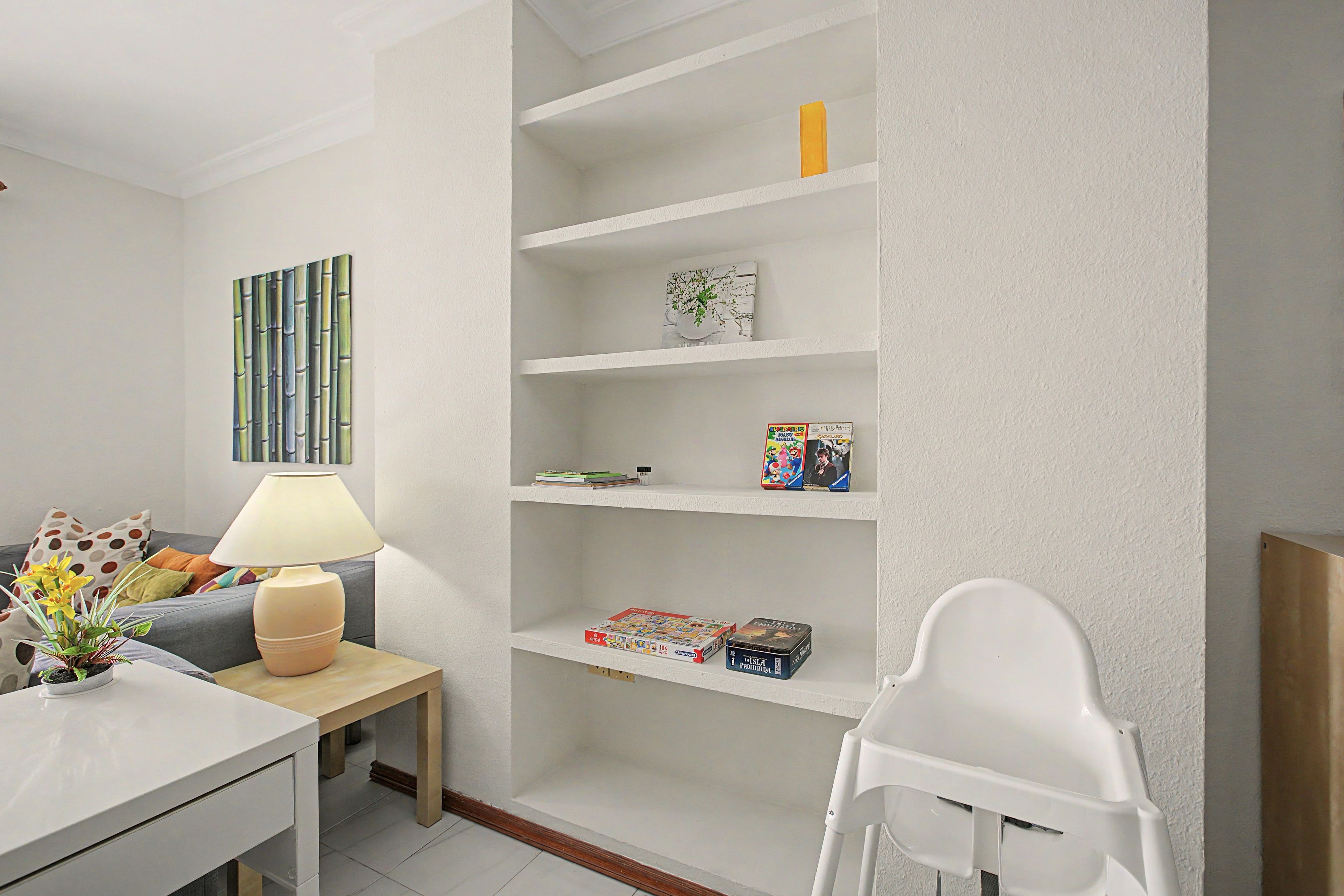 Una sala de estar moderna con un sofá blanco, una mesita de noche con una lámpara, una estantería y una silla blanca.