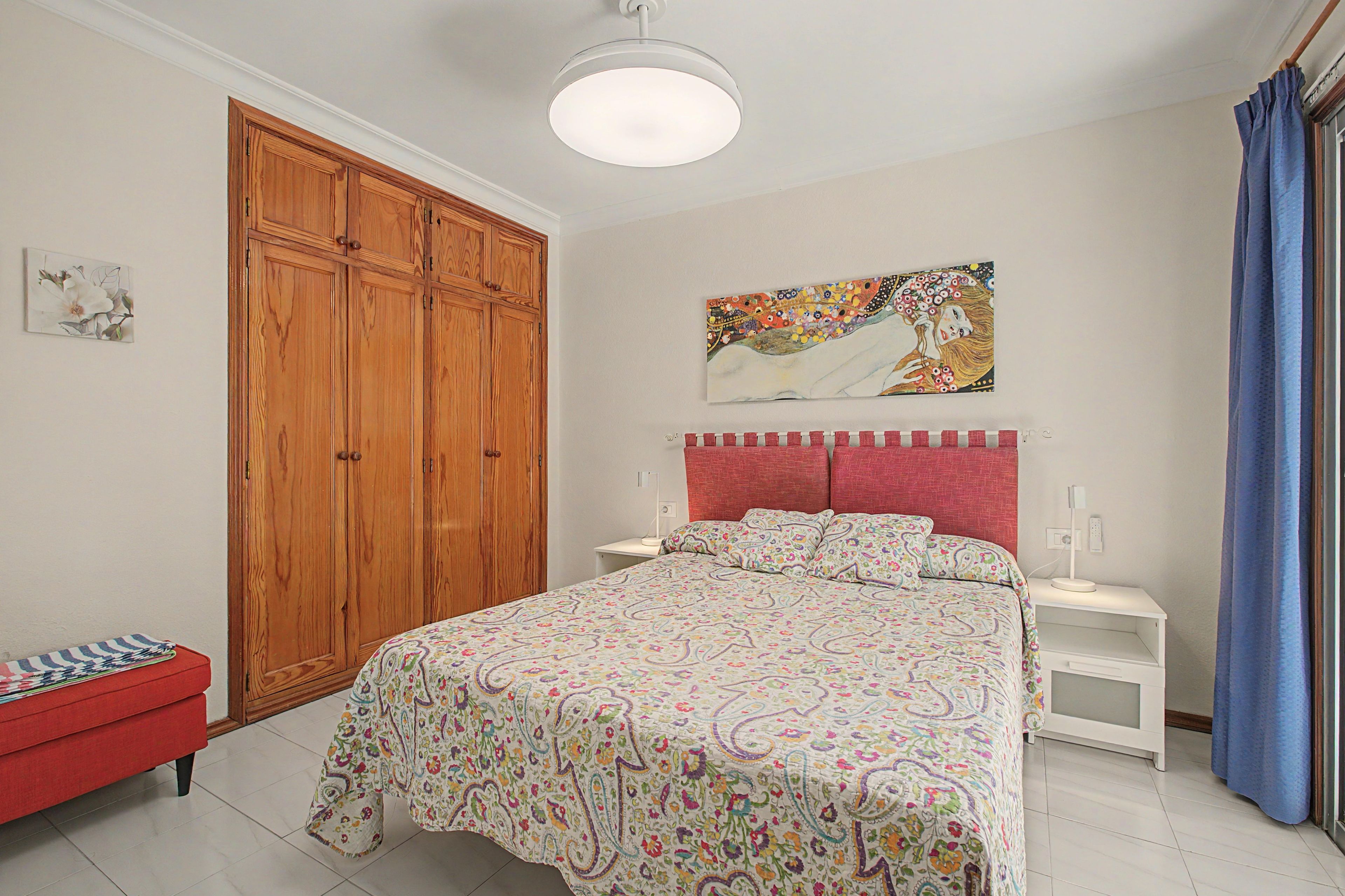 Ein Schlafzimmer mit einem Bett, einem Nachttisch, einer roten Bank, einem Holzschrank und einem Bild an der Wand.