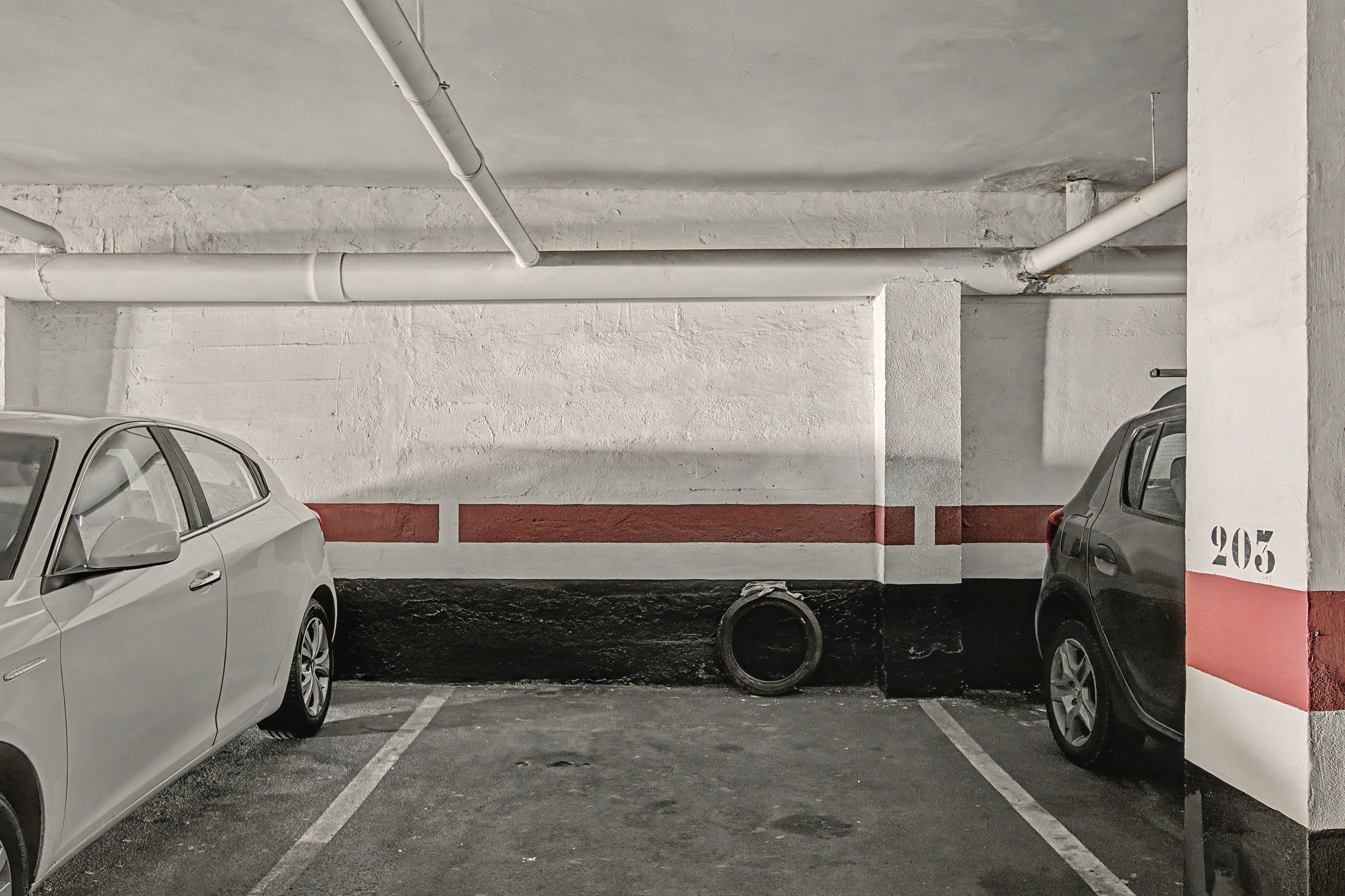 Un estacionamiento con dos coches aparcados, paredes de hormigón y el número '203' visible a la derecha.