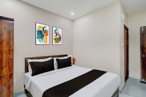 A hotel room with a bed, two framed artworks on the wall, and a wooden door. - Townhouse Chaitanyapuri Metro Station (Hyderabad)