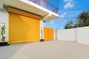 Un bâtiment avec un volet jaune fermé, un mur en briques blanches et un balcon doté de balustrades violettes.