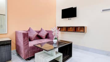 Un salon moderne comprenant un canapé, une table basse, un téléviseur à écran plat et une étagère fixée au mur.