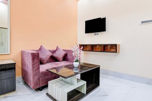 Un salon moderne comprenant un canapé, une table basse, un téléviseur à écran plat et une étagère fixée au mur.
