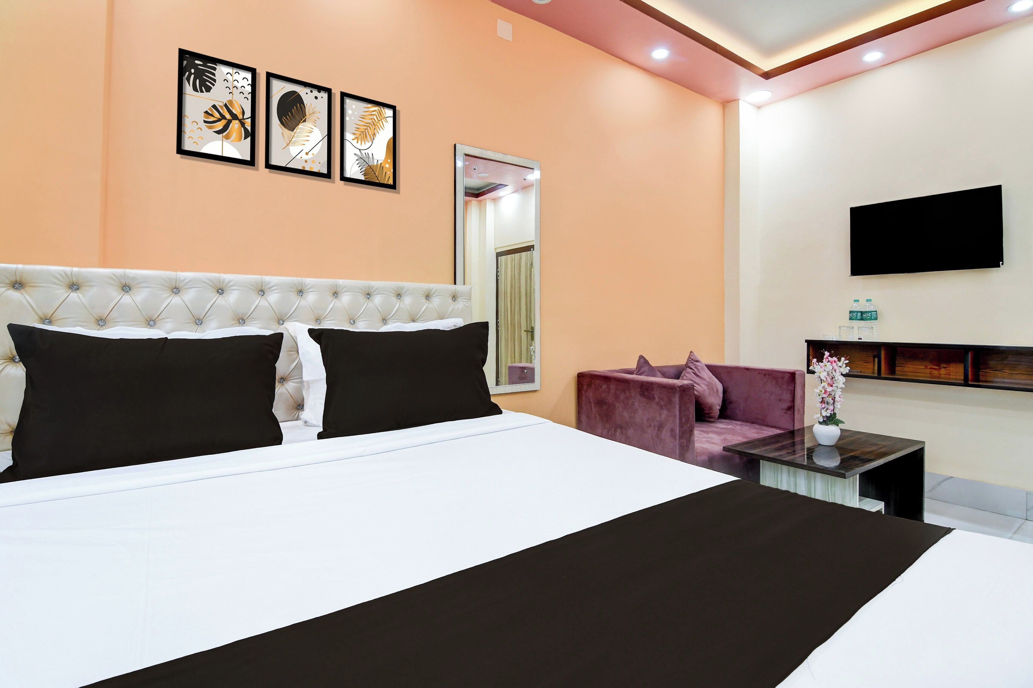 A hotel room with a large bed, a sofa, a TV mounted on the wall, and framed artwork above the bed.
