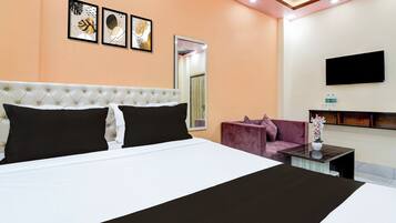 A hotel room with a large bed, a sofa, a TV mounted on the wall, and framed artwork above the bed.
