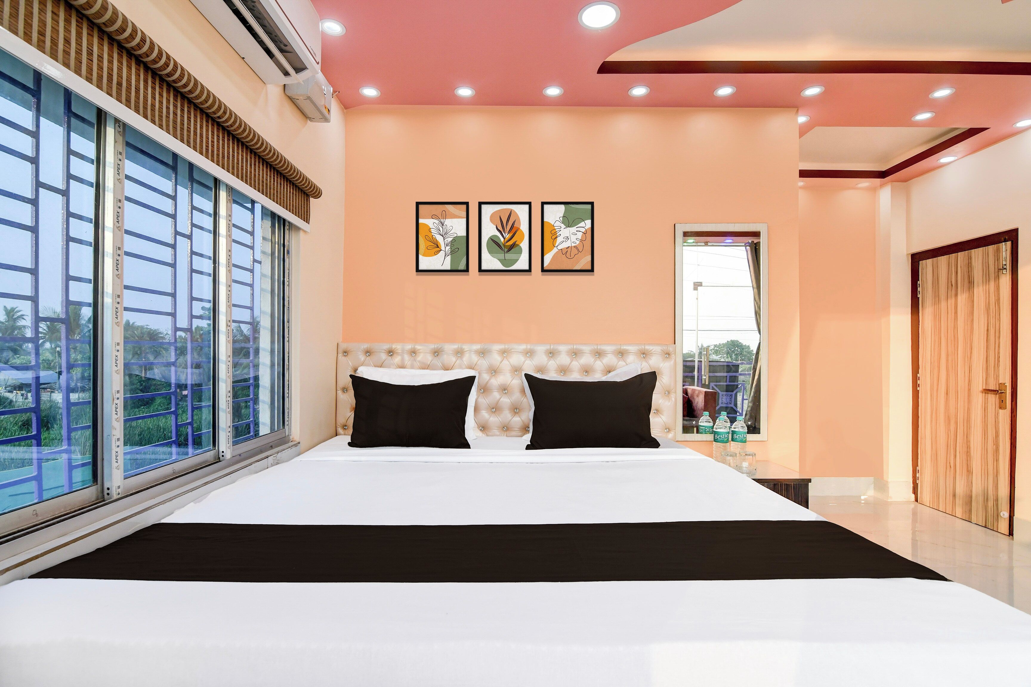 Une chambre d’hôtel avec un grand lit, une fenêtre avec des stores, un plafond doté d’un éclairage encastré et une porte.