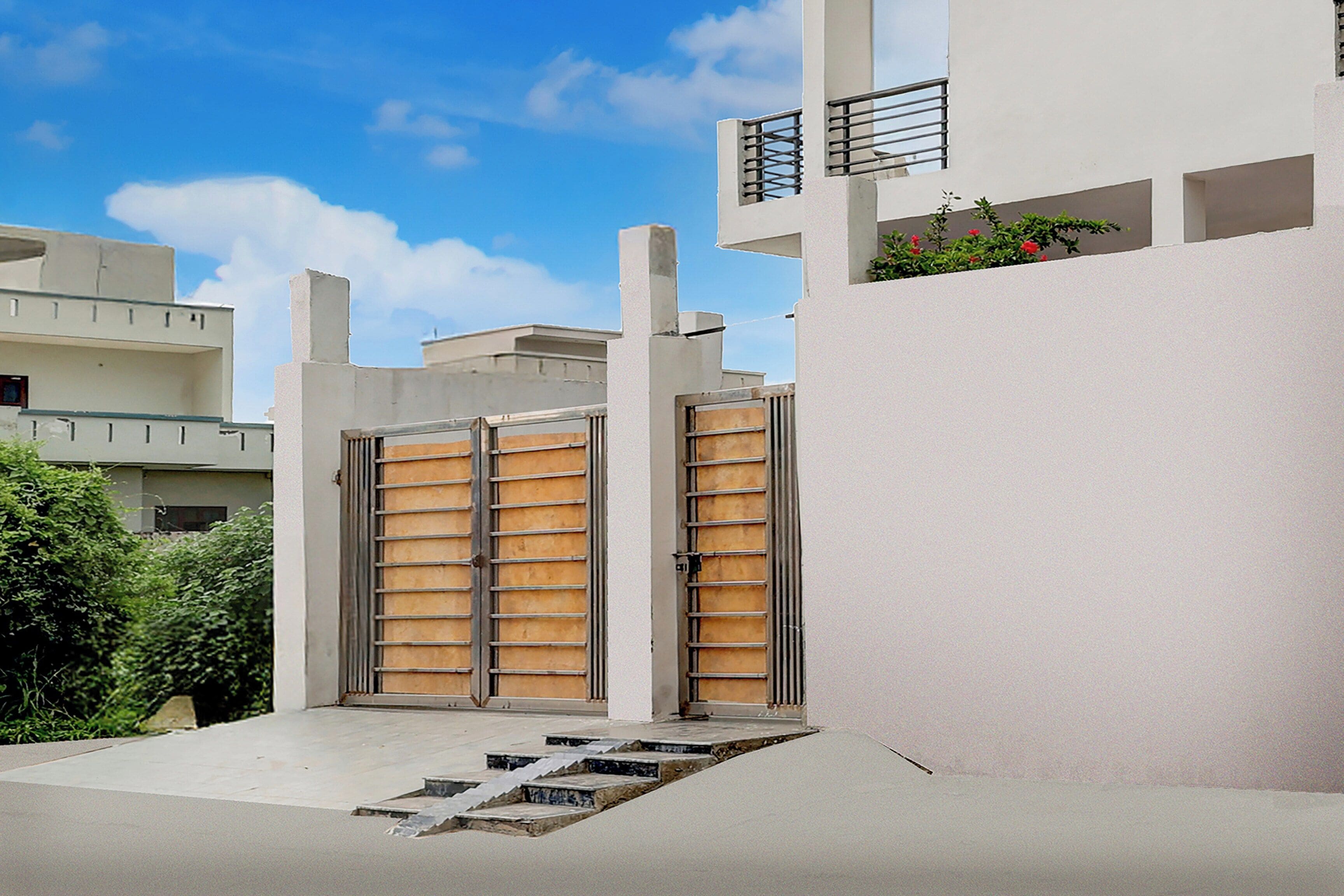 A modern building with a white facade, a gated entrance, and a small outdoor area with steps leading to a door.