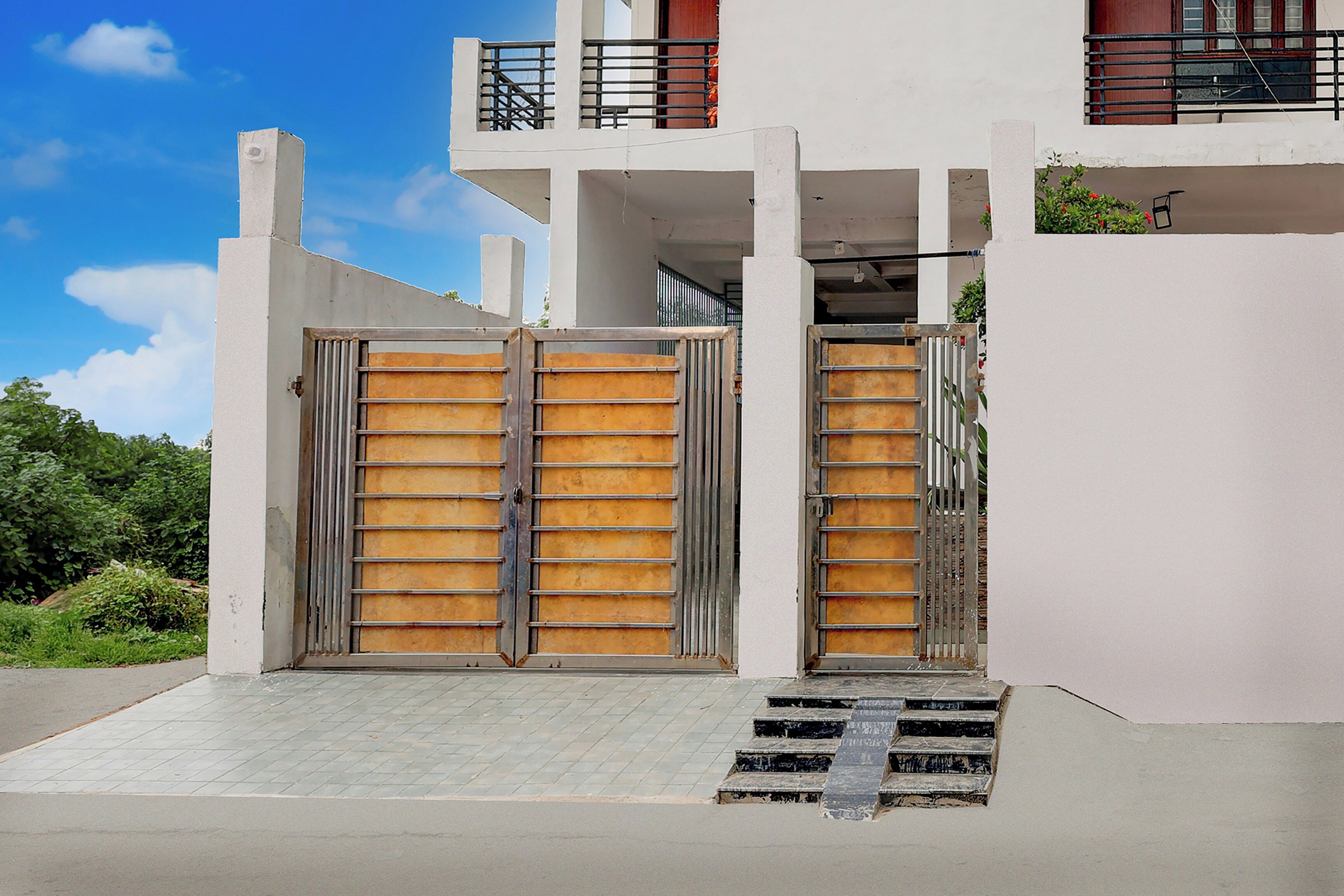A modern building with a gated entrance, a staircase leading to a balcony, and a clear sky.