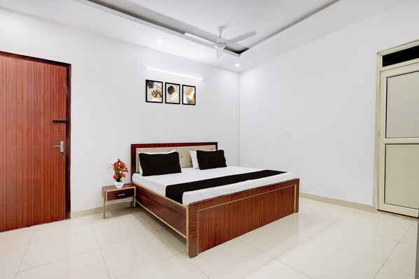 A bedroom with a wooden bed, white walls, a ceiling fan, and three framed pictures on the wall.