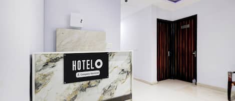 Zona de recepción de un hotel con mostrador de mármol, cámara de seguridad y una puerta cerrada.