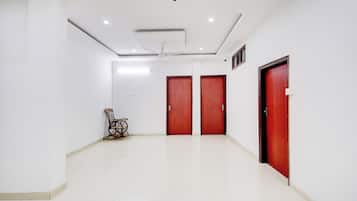 Un hall d’entrée spacieux aux murs blancs, avec deux portes en bois, un ventilateur de plafond et une chaise.
