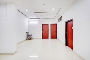 A spacious hallway with white walls, two wooden doors, a ceiling fan, and a chair.