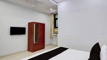 A bedroom with a bed, a wardrobe, a television, and a ceiling fan.