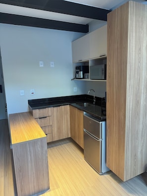 A modern kitchen with wooden cabinets, a stainless steel refrigerator, and a black countertop.