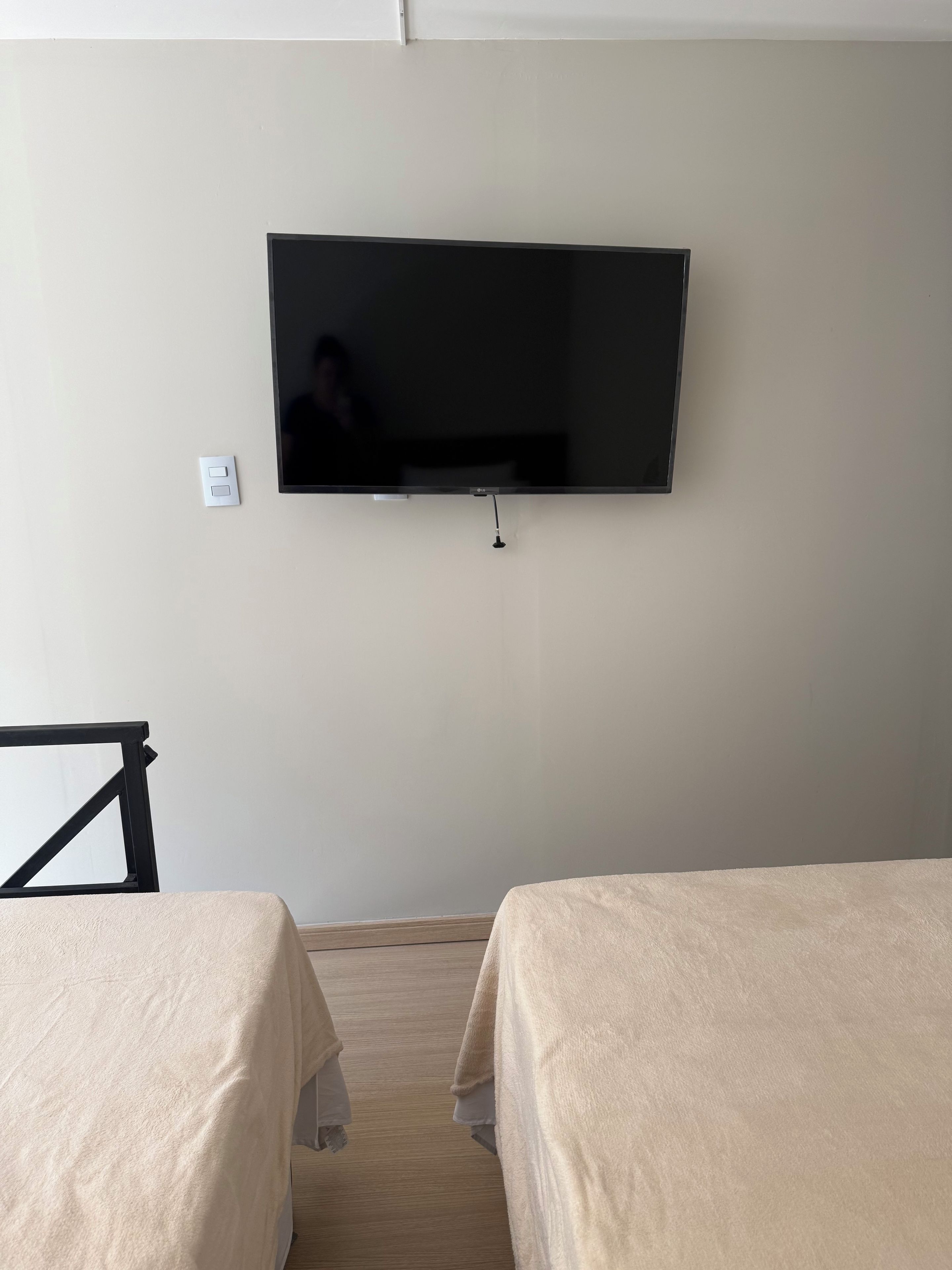 Une chambre dotée d’un téléviseur à écran plat fixé au mur, de deux lits avec une literie beige et d’un plancher en bois.