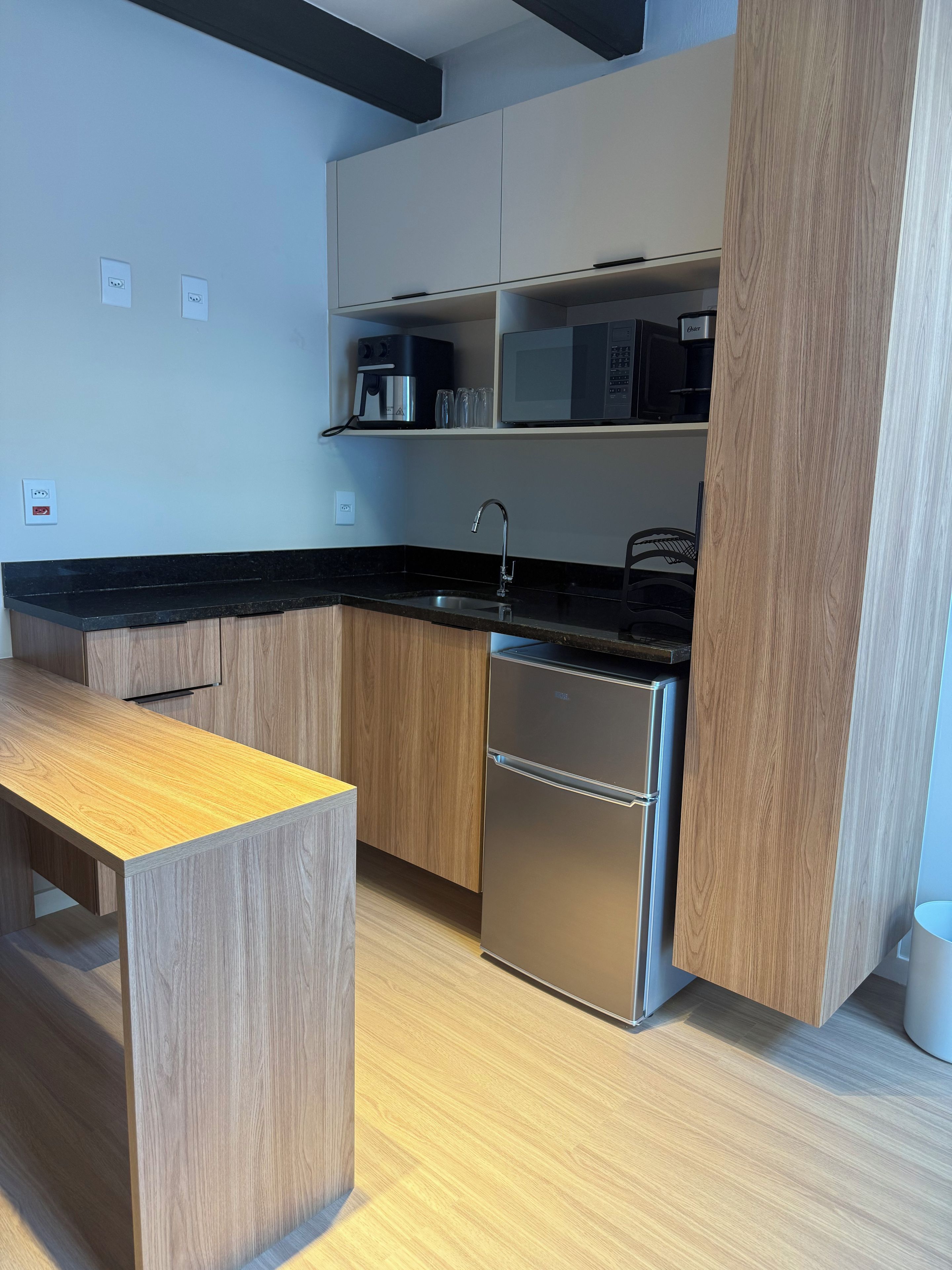 Une cuisine moderne avec des meubles en bois, un réfrigérateur en acier inoxydable et un plan de travail noir.