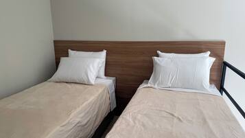 Een kamer met twee eenpersoonsbedden, elk met een houten hoofdbord en wit beddengoed.