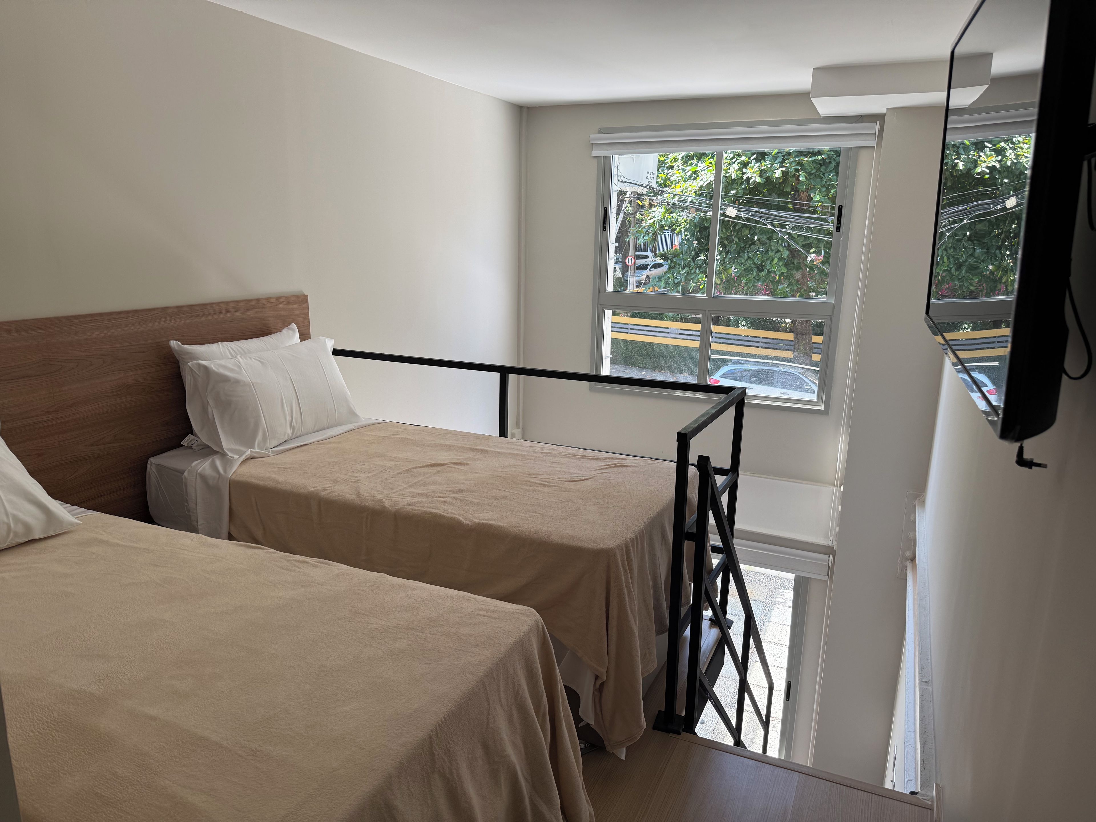 Une chambre d’hôtel avec deux lits, une fenêtre donnant sur la rue et un appareil fixé au plafond.