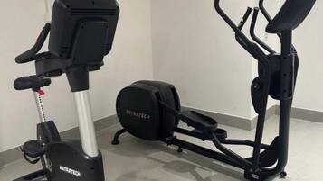 A stationary bike and an elliptical machine in a room with white walls and a tiled floor.