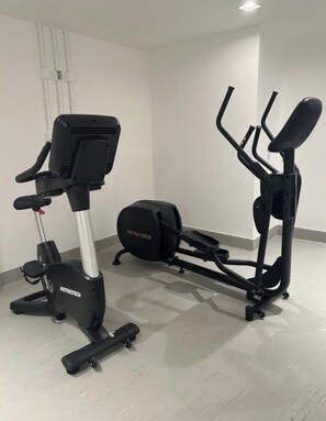A stationary bike and an elliptical machine in a room with white walls and a tiled floor.