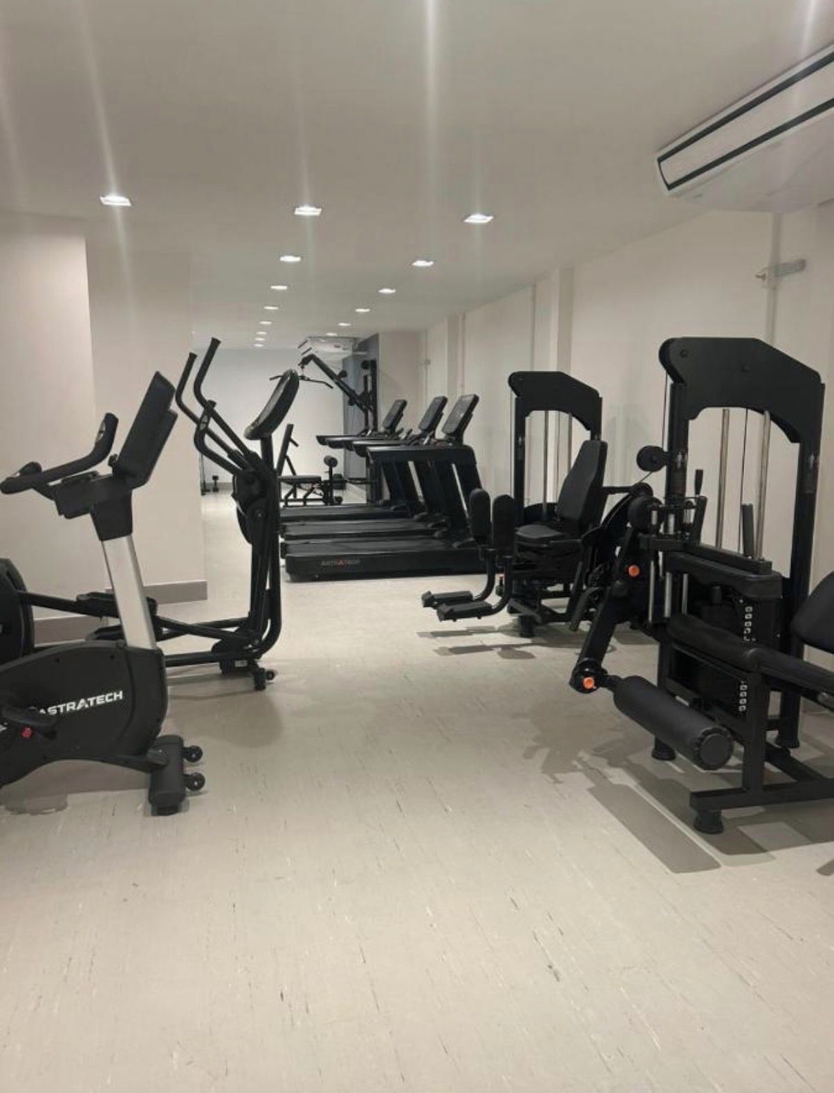 Een fitnessruimte met diverse trainingsapparaten, waaronder loopbanden, elliptische trainers en krachttrainingsapparaten.