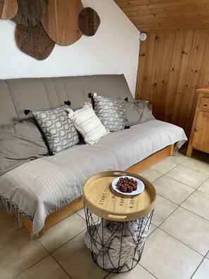 A cozy room with a sofa, patterned pillows, a round wooden table with a plate of food, and a wall-mounted light fixture. - The Ski Apartment (4 People) Valley view, close to the slopes and downtown. (Saint-Gervais-les-Bains)