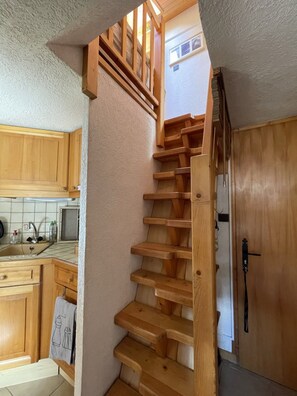 A wooden staircase leading to an upper level, a kitchen with wooden cabinets, and a door with a handle. - The Ski Apartment (4 People) Valley view, close to the slopes and downtown. (Saint-Gervais-les-Bains)