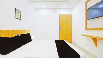 A hotel room with a bed, a wooden headboard, a door, a wall-mounted TV, and a framed picture.