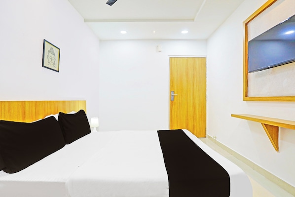 A hotel room with a bed, a wooden headboard, a door, a wall-mounted TV, and a framed picture.