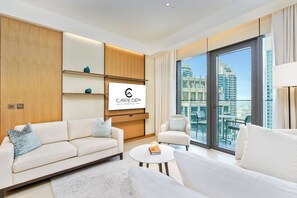 A modern living room with a sofa, armchair, and coffee table, a mounted TV, and a city view through large windows. - Bright apartment in brilliant Dubai with cool AC for your stay (Dubai)