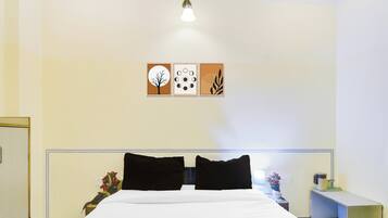 Habitación de hotel con una cama, dos almohadas negras, una mesita de noche con lámpara, un florero con flores y decoración en la pared sobre la cama.