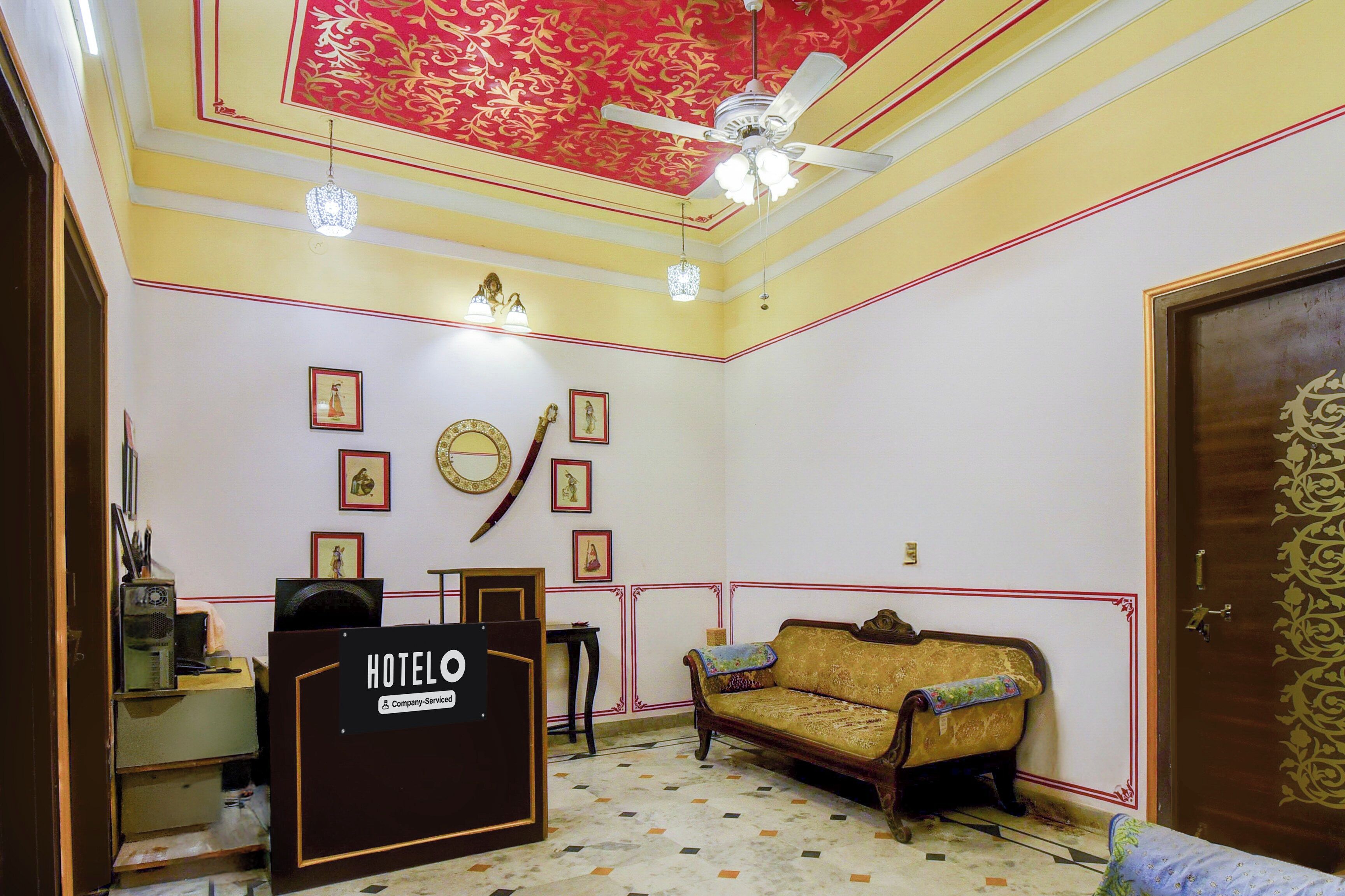 Habitación de hotel con recepción, sofá, ventilador de techo y cuadros en las paredes.