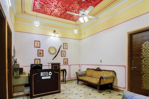 Habitación de hotel con recepción, sofá, ventilador de techo y cuadros en las paredes.