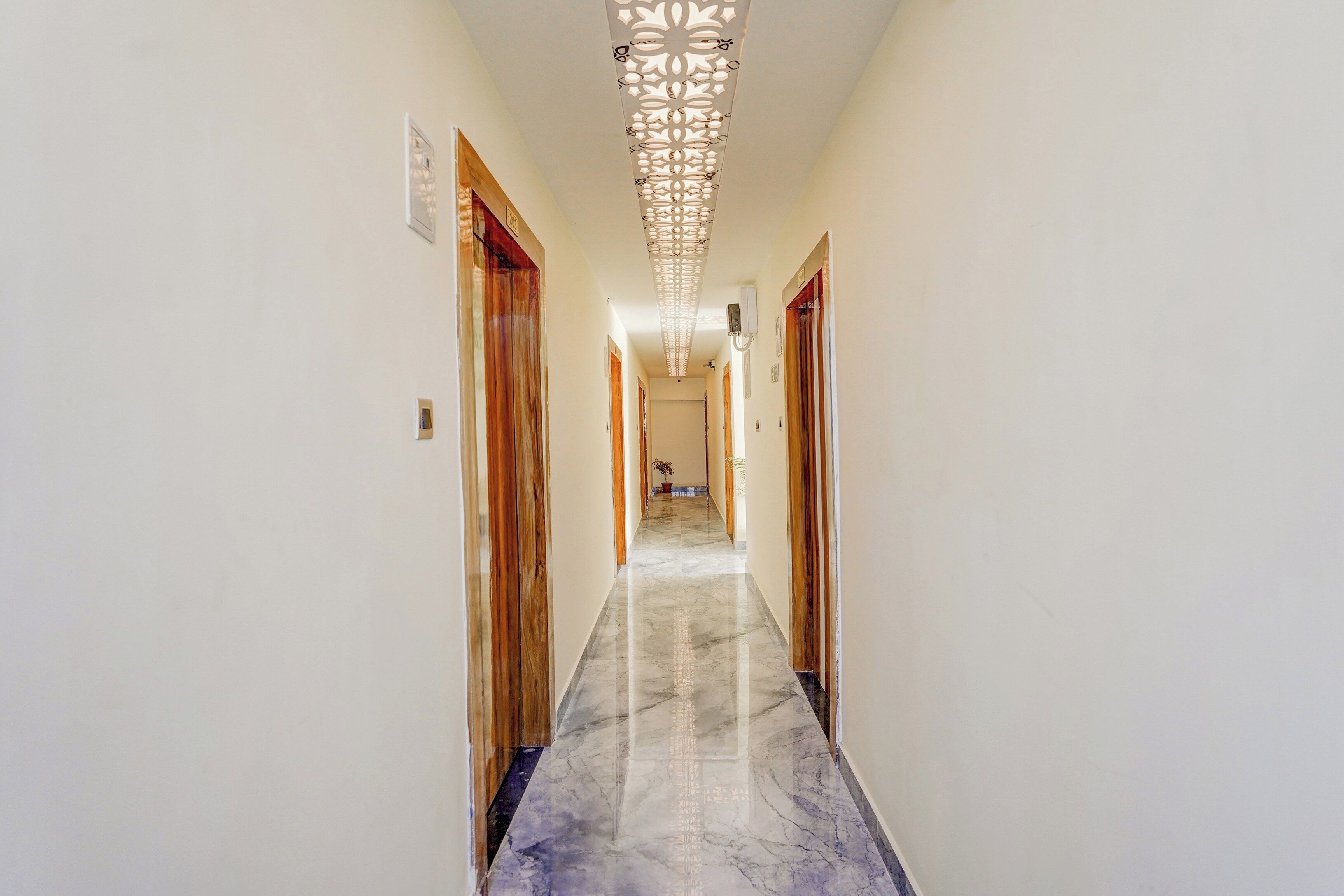 Un couloir avec des portes en bois, un sol en marbre et un luminaire décoratif au plafond.