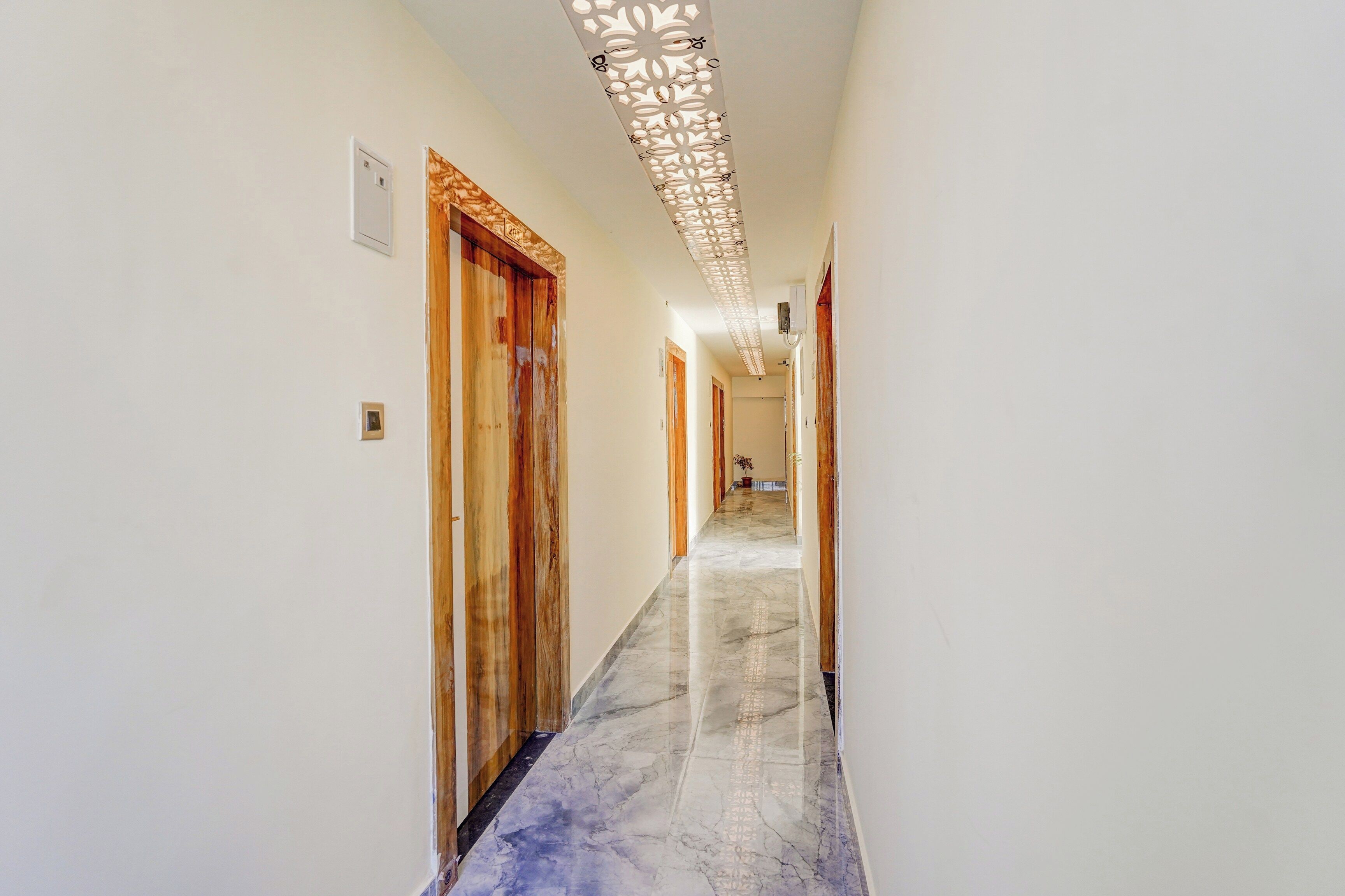 Ein Korridor mit Holztüren, einem Marmorboden und einer dekorativen Deckenleuchte.