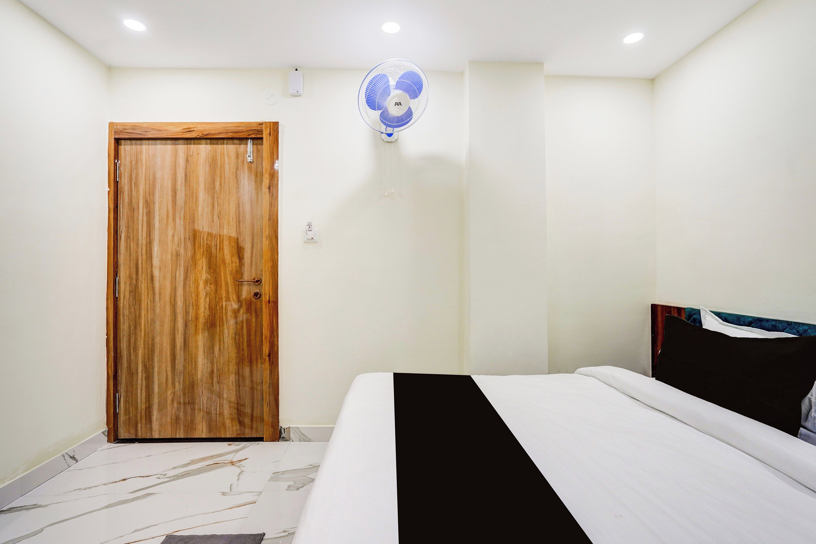 A bedroom with a wooden door, a bed with a black and white bedspread, and a ceiling fan.
