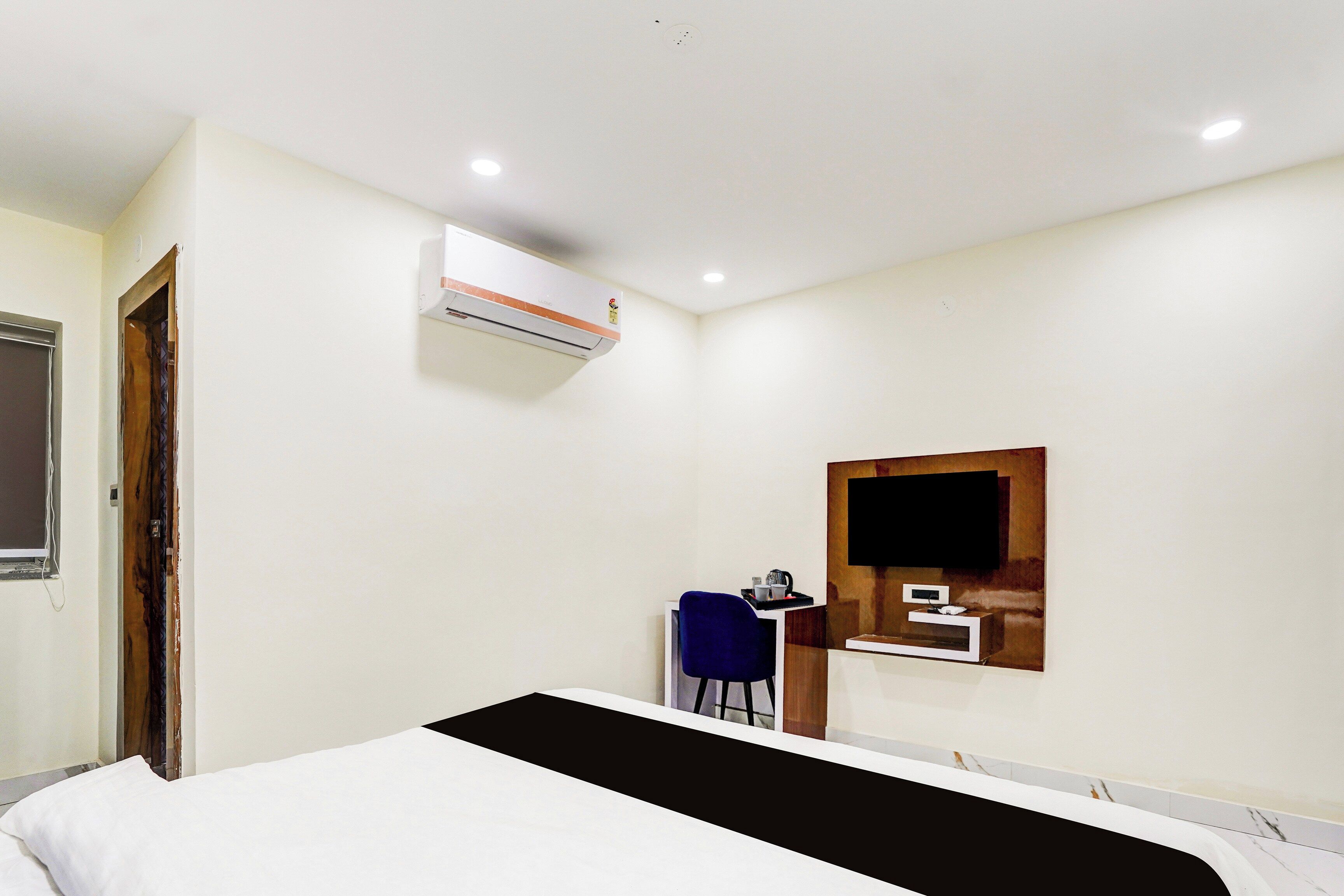 Ein Hotelzimmer mit einem Bett, einem Schreibtisch mit Stuhl, einem an der Wand befestigten Fernseher und einer Klimaanlage.