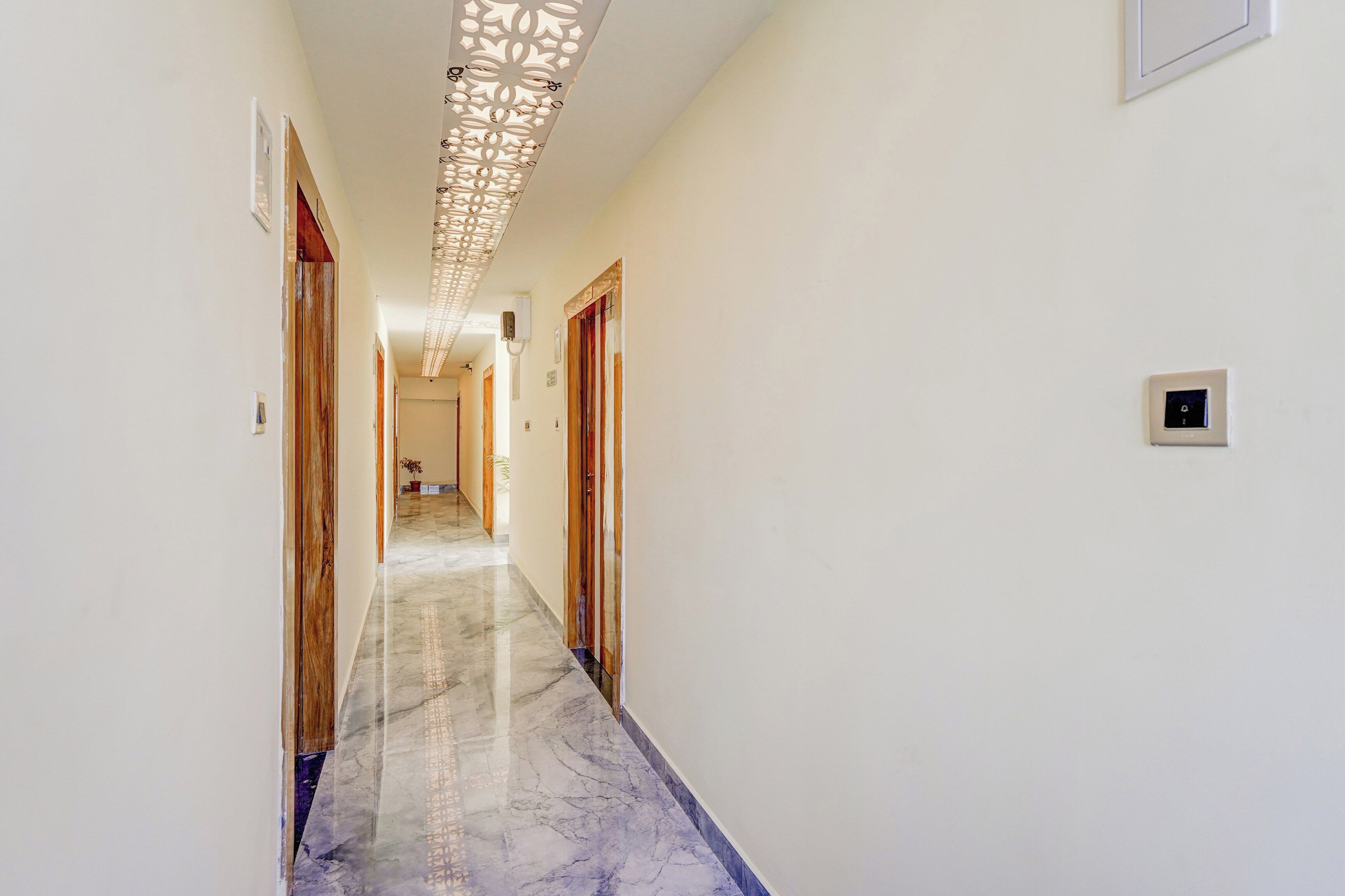 Un pasillo con piso de mármol, puertas de madera y un aplique decorativo en el techo.
