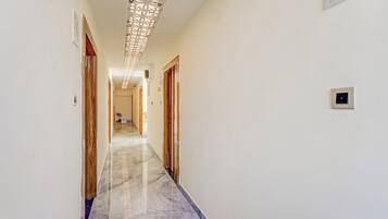 Un pasillo con piso de mármol, puertas de madera y un aplique decorativo en el techo.