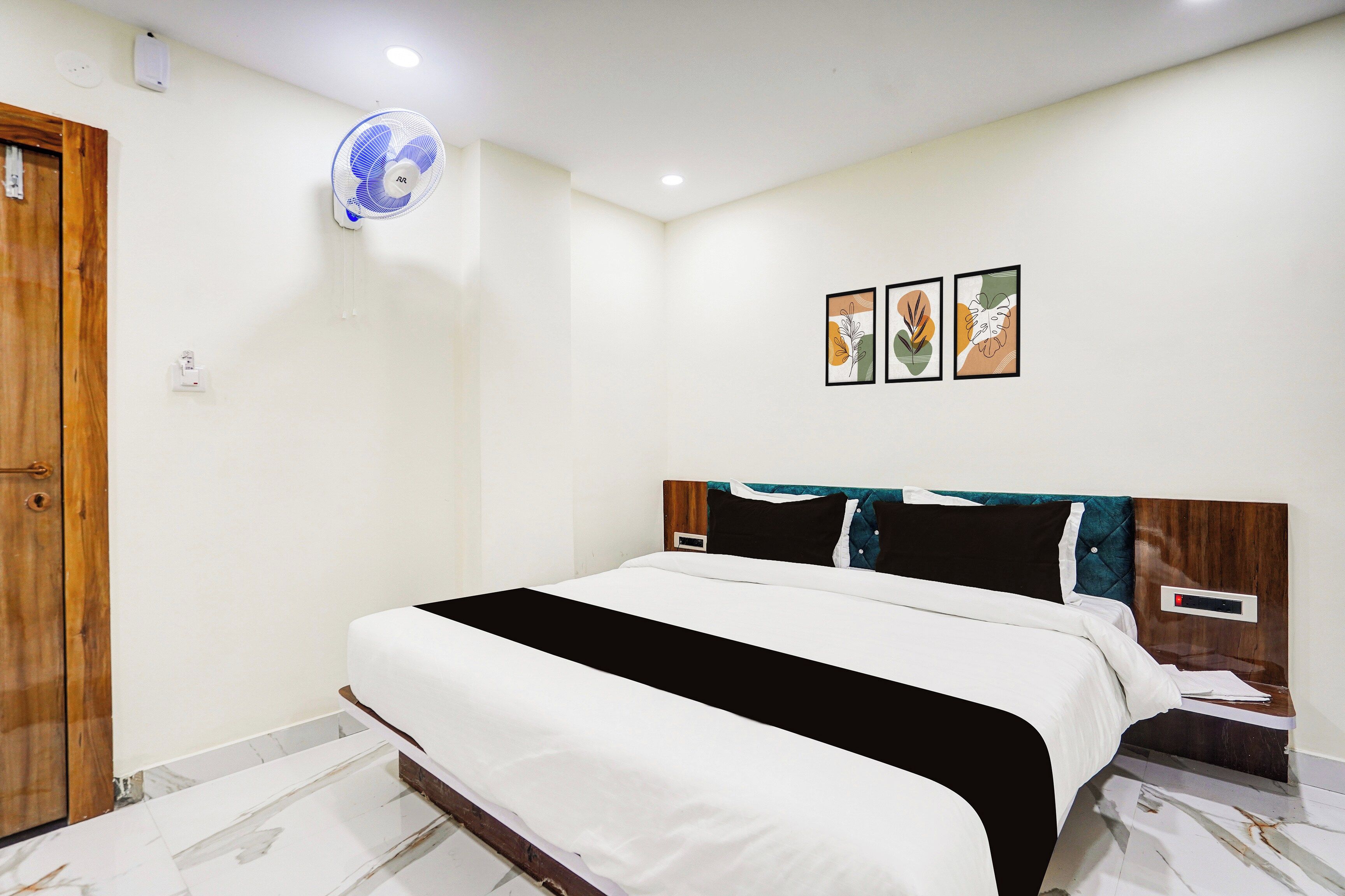Une chambre à coucher avec un lit, un ventilateur fixé au mur et trois œuvres d’art encadrées.