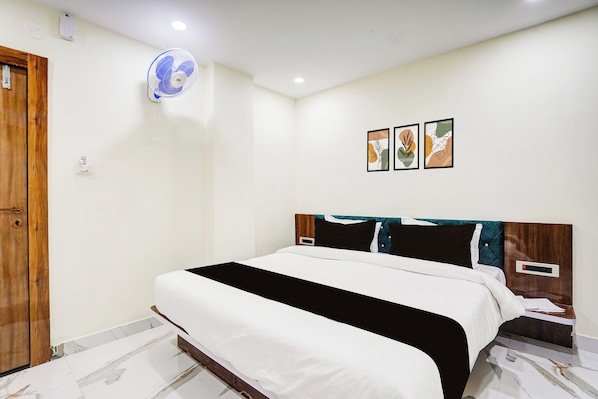 A bedroom with a bed, a wall-mounted fan, and three framed artworks.