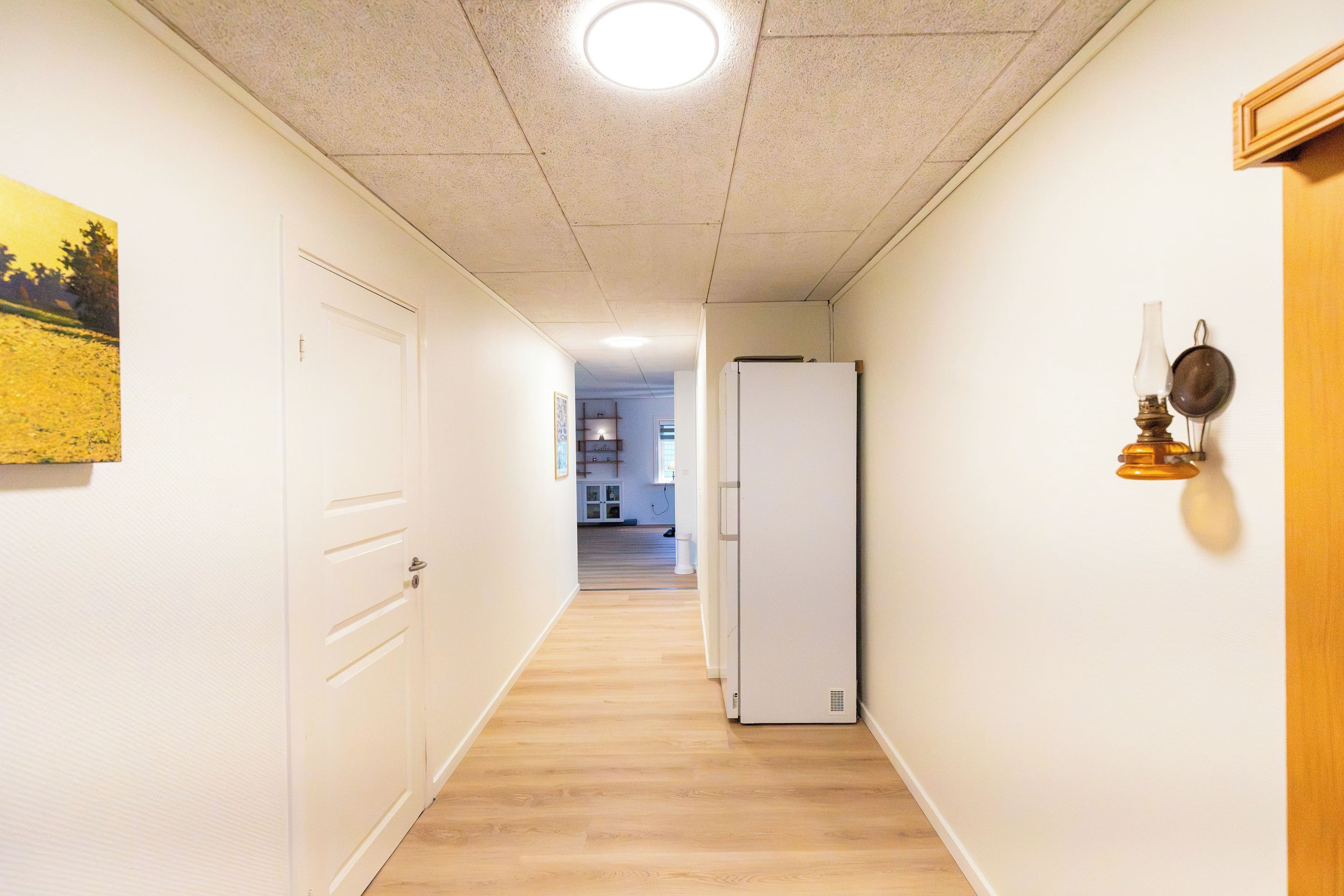 A narrow hallway with a wooden floor, white walls, and a white door at the end.