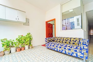 Habitació amb sòl motllurat, un sofà, plantes en testos, un armari i una porta amb un calendari.