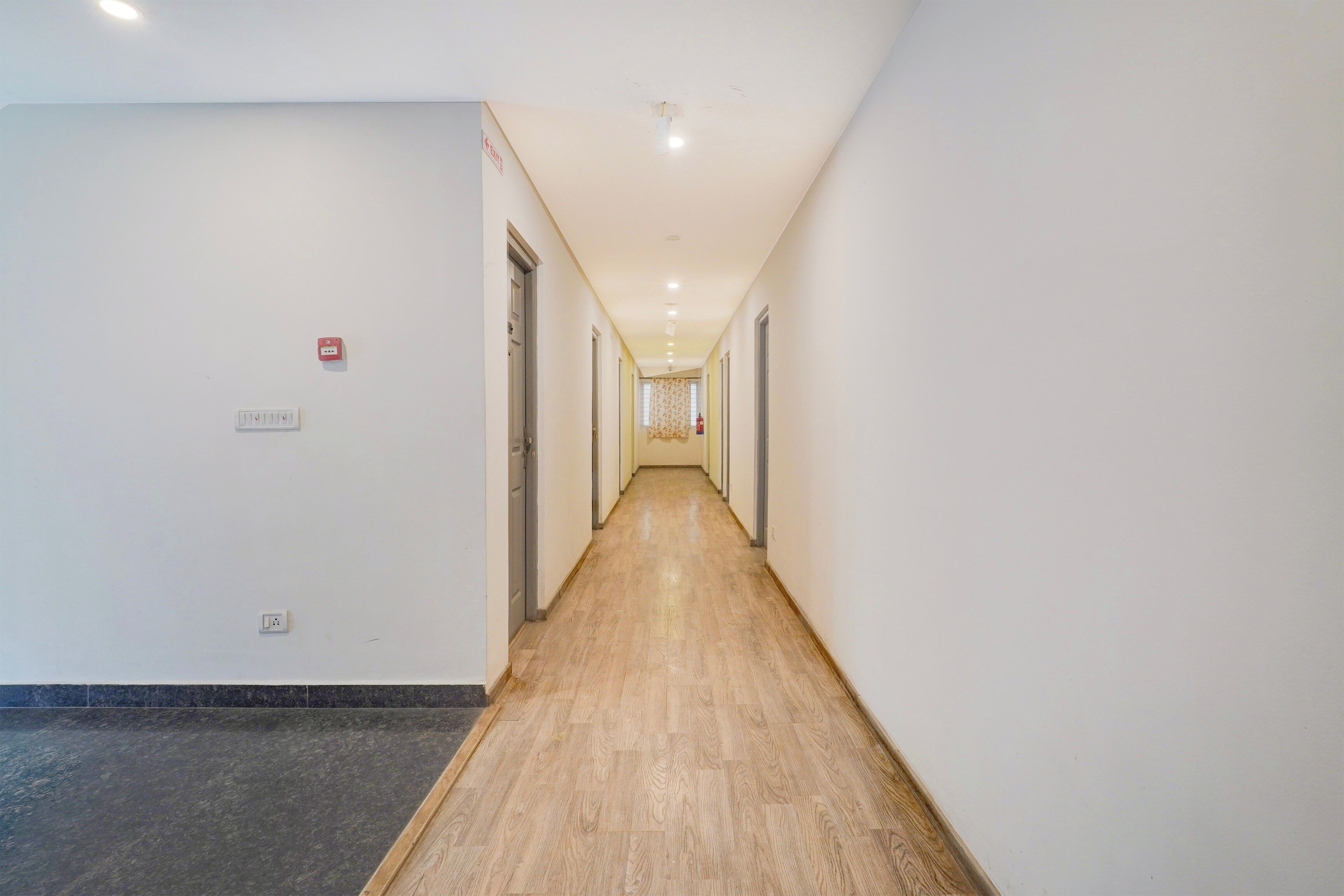 Un largo y estrecho pasillo con suelo de madera, paredes blancas y puertas a ambos lados.