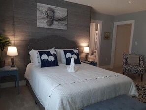 Ein Schlafzimmer mit einem großen Bett, zwei Nachttischen inklusive Lampen, einem Sessel und einem Wandbild.