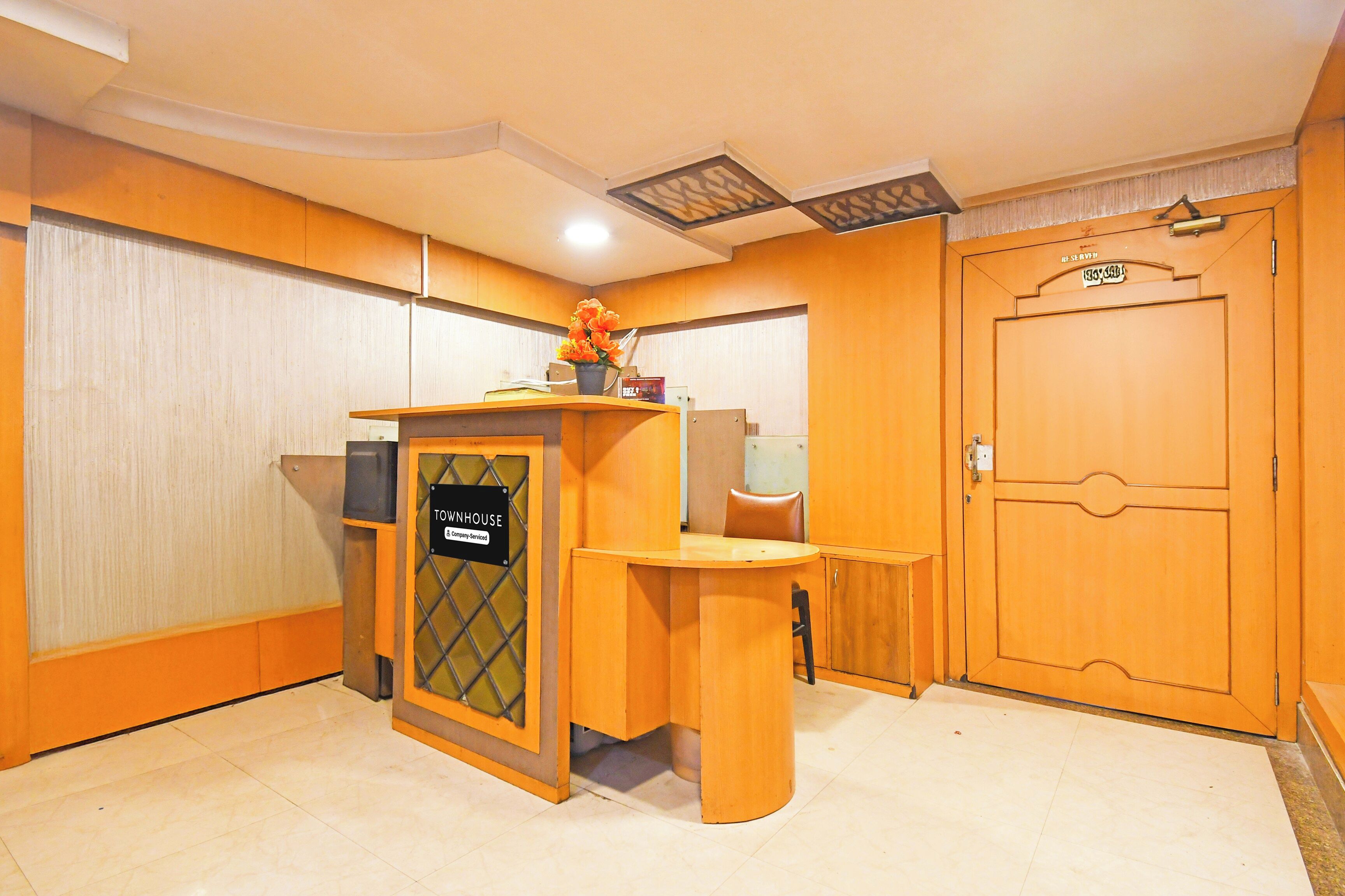A reception area with a wooden desk, a sign reading 'TOURNHOUSE & Company Serviced,' and a door with a number plate.