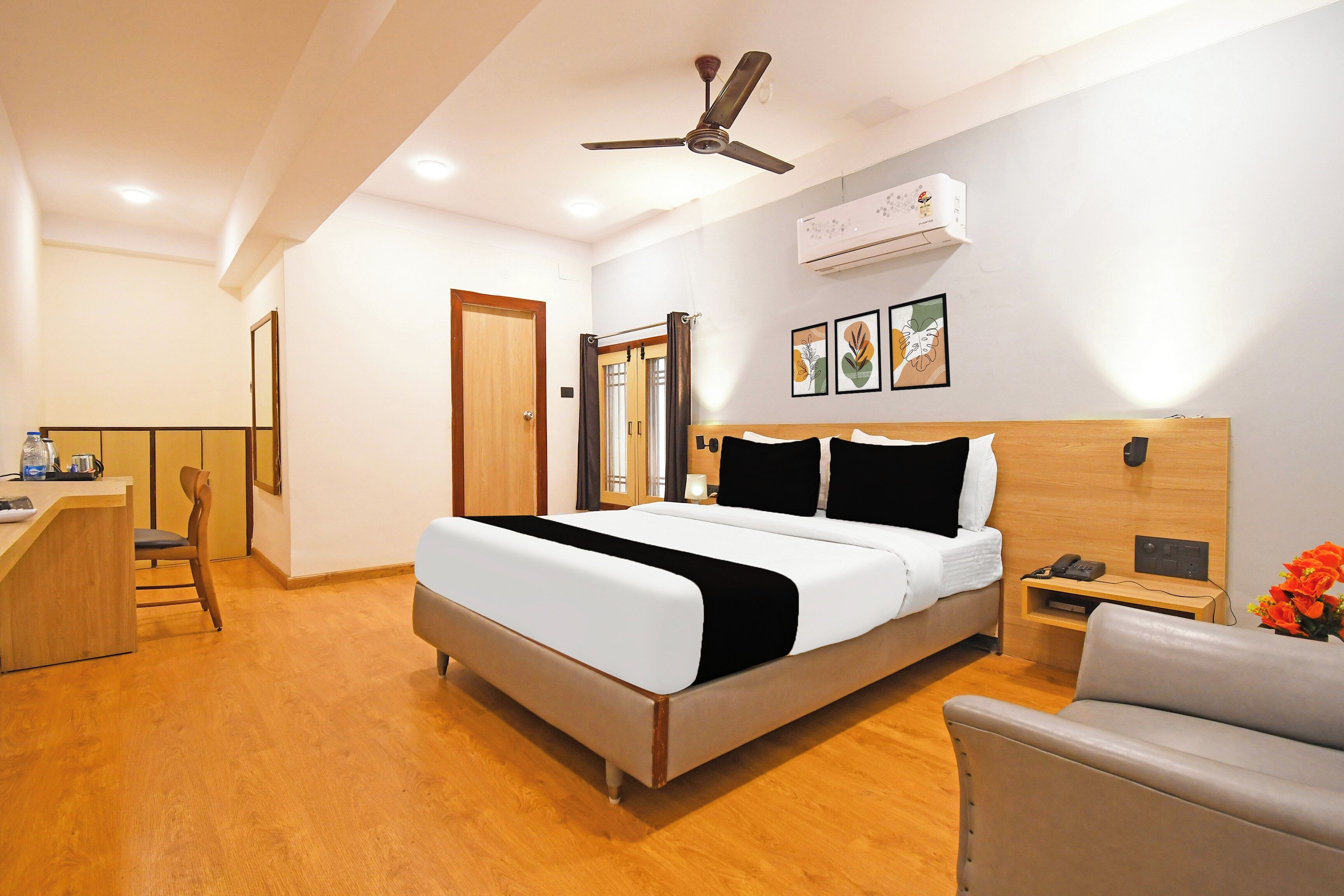 Habitación de hotel con cama, escritorio, silla, mesita de noche con teléfono y ventilador de techo.