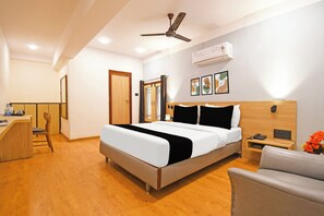 Habitación de hotel con cama, escritorio, silla, mesita de noche con teléfono y ventilador de techo.