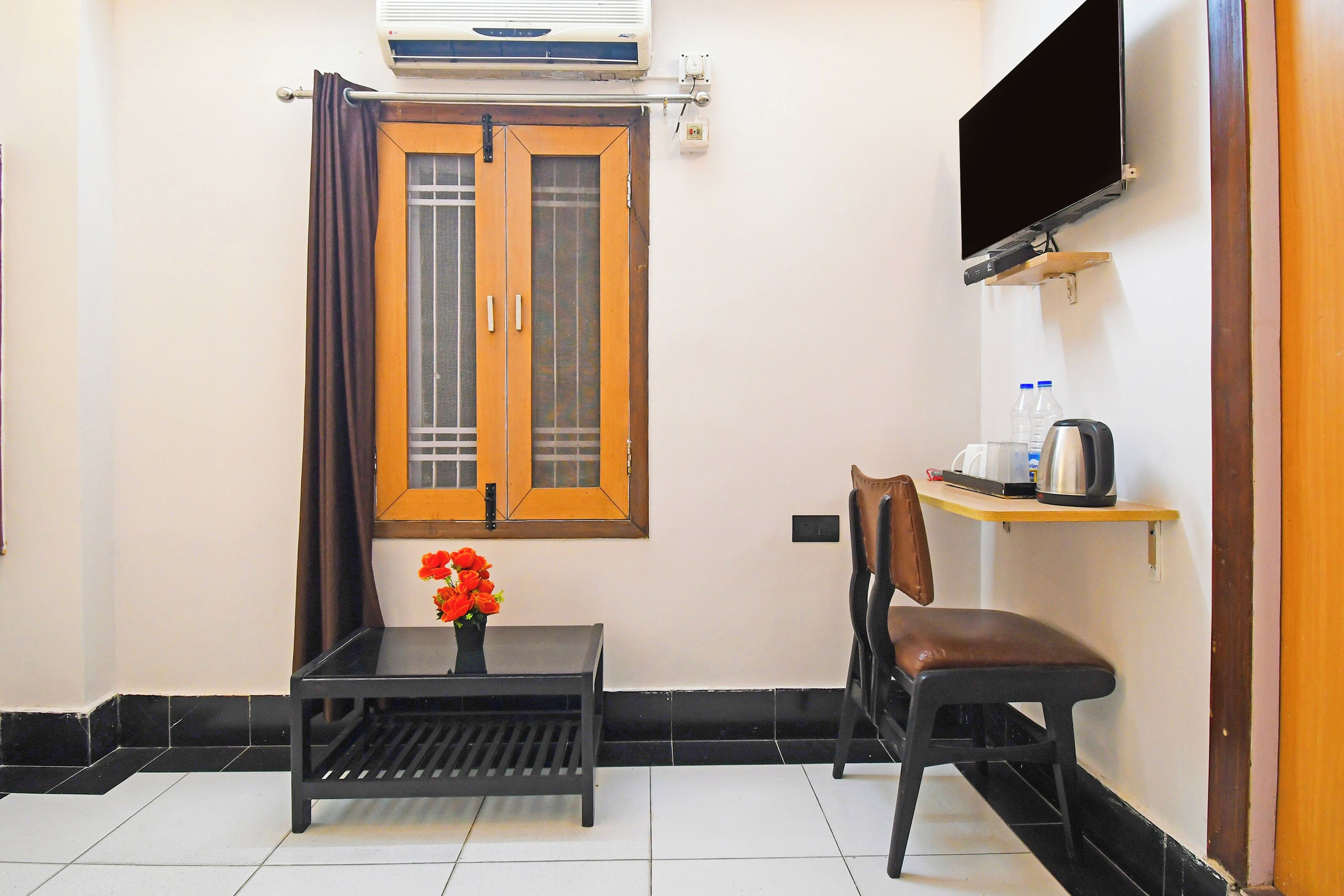 A small room with a single table, a chair, a TV mounted on the wall, and a window with curtains.