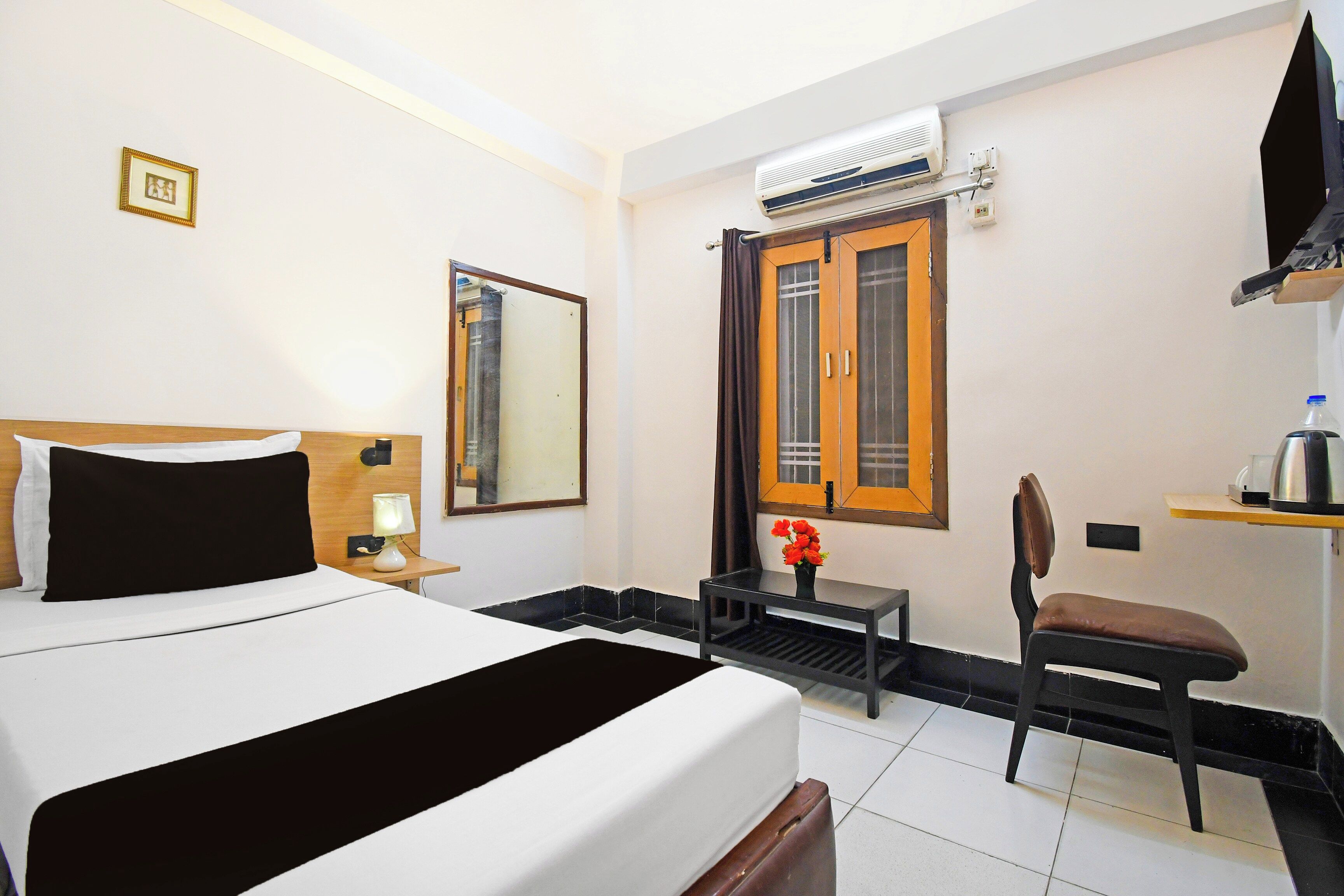 A hotel room with a bed, a desk, a chair, a mirror, an air conditioner, and a TV.
